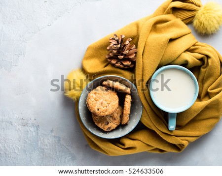Mug of tea with milk and cookies with chocolate chips in a soft yellow winter scarf on gray background. Coffee break for home relax. Top view
