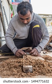 MUHARRAQ, BAHRAIN - FEBRUARY 24, 2017: A Kneeling Migrant Worker From India Shaves Wood With A Spokeshave Tool As He Fashions A Door Frame.