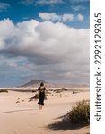 Mujer con vestido andando por el desierto de las dunas de corralejo en Fuerteventura, en verano, durante un viaje vacacional por las islas canarias.