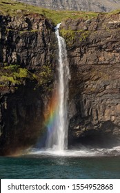 Mulafossur Waterfall crashing into the ocean and creating a rainbow at Gasadalur, Vagar, Faroe Islands. September 2019.  