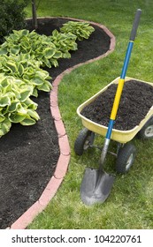 Mulch Bed Around The House And Wheelbarrow Along With A Shovel.