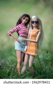 Mulhouse - France - 26 April 2021 - Portrait of blond and brunette barbie dolls wearing orange summer dress and blue jeans mini skirt  standing in a public garden