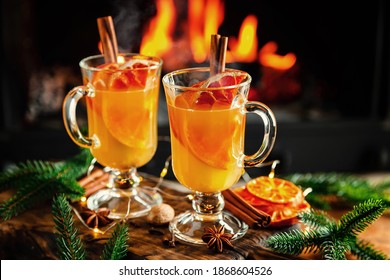 Mulled Cider Glasses On The Background Of Fireplace Fire. Hot Mulled Spiced Apple Cider Cocktail For Winter Or Autumn Time.