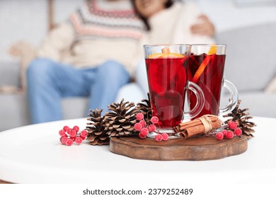 Mulled wine with cinnamon and Christmas decorations on white table in living room, closeup