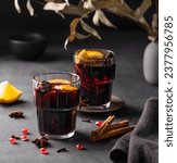 Mulled wine with orange, apple, pomegranate and cinnamon in glasses on a dark background. The concept of a traditional winter hot drink with spices and fruits for the holiday.
