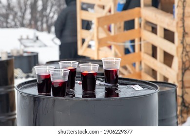 Mulled Wine Outside In Plastic Glasses On Black Metal Barrel In Winter Near A Mountain Chalet