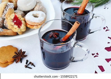 Mulled wine in two glass mugs with cinnamon sticks, star anise, cloves and gingerbread cookies on plate.