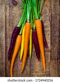 Multi Colored Carrots With Stems On Rustic Wood Table.