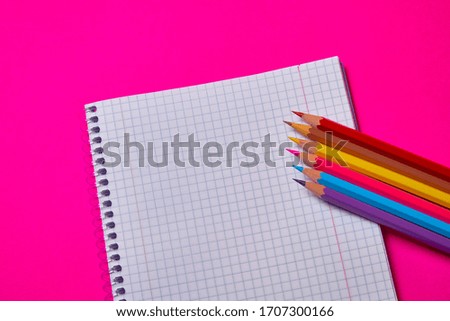 Multi colored crayons and binder notepad at magenta background with copy space