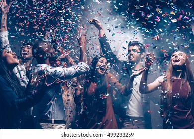 Multi colored fun. Group of beautiful young people throwing colorful confetti while dancing and looking happy