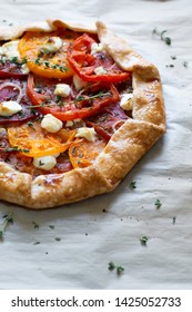 A Multi Colored Heirloom Tomato Galette With Thyme And Feta Cheese On Parchment Paper