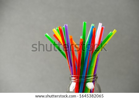 Multi colored plastic straws in a jar in front of a grey background.