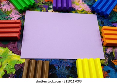 Multi Colored Rectangle Pieces Of Plasticine, Piece Of  A Pale Purple Paper Lie On A Cardboard With Plasticine Abstract Painting, Background