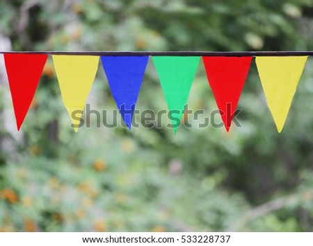 Multi Colored Triangular Flags Hanging in the Sky at an Outdoor against the backdrop of a green grass