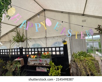 A Multi Coloured Bunting Sign Says Happy Easter Hung In A Marquee With Daffodils In The Background. Celebration.Public Holiday