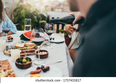 Multi cultural group of people dining together outdoors, Man pouring red wine into glass during cozy family dinner with festive table served with mediterranean food, Friendship Dinner Hanging Out  - Powered by Shutterstock