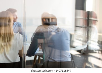 Multi Ethnic Business People Negotiating Sitting At Conference Table, Diverse Staff Employees Talk At Team Private Meeting In Modern Office Boardroom, Colleagues Group Collaborate, View Through Glass