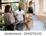 Multi ethnic businesspeople talking and smiling during a work break in the hallway of a modern coworking with plants and bicycle, enjoying a moment of social inclusion and diversity