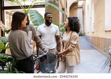 Multi ethnic businesspeople talking and smiling during a work break in the hallway of a modern coworking with plants and bicycle, enjoying a moment of social inclusion and diversity - Powered by Shutterstock