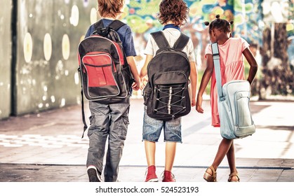 Multi ethnic classmates walking in schoolyard, seen from behind.