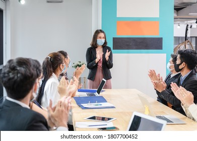 Multi Ethnic Colleagues Celebrating With Applauding The Female Executive While Meeting In New Normal Office. Business Team Wearing Face Mask While Pandemic Of Coronavirus, Covid-19