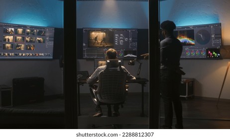 Multi ethnic colorist and film maker edit video and make color grading in program. Process of colour correction for movie post production in modern studio. Multiple monitors with action film footage. - Shutterstock ID 2288812307