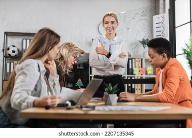 Multi Ethnic Company Workers Sitting At Desk With Modern Devices, Preparing Financial Report And Listening Speech Of Their Young Female Boss. Concept Of Technology And Cooperation.