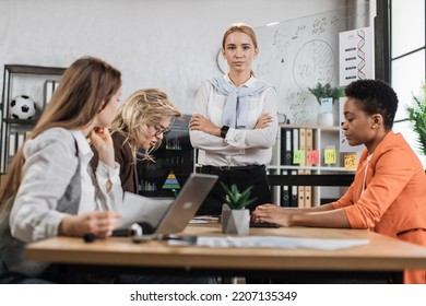 Multi Ethnic Company Workers Sitting At Desk With Modern Devices, Preparing Financial Report And Listening Speech Of Their Young Female Boss. Concept Of Technology And Cooperation.