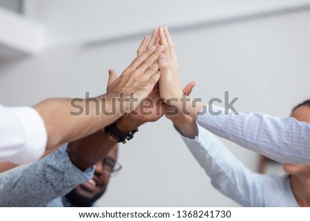 Multi ethnic corporate office business team winners join hands give high five together, success gesture, startup triumph, professional victory, teamwork accomplishment teambuilding concept, close up