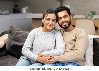 Multi ethnic couple in love rent a house together. Happy Indian newlyweds moved in new apartment, sitting at the sofa in embraces, looking at the camera - Powered by Shutterstock