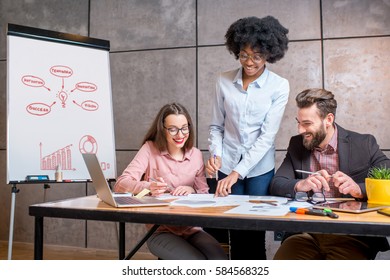 Multi ethnic coworkers working together with documents and laptop at the workplace with whiteboard on the grey wall background - Shutterstock ID 584568325