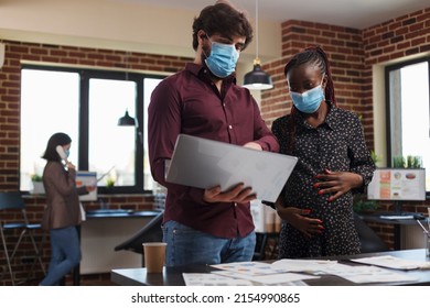 Multi Ethnic Diverse Office Workers Wearing Facemasks Against Coronavirus Analyzing Financial Data And Reviewing Client Portfolio. Expectant Mother Finance Advisor Looking Over Startup Project Ideas.