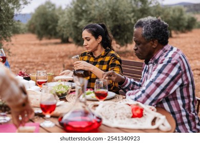 Multi ethnic farmers are having lunch together in an olive grove, pouring olive oil and enjoying wine after harvesting olives - Powered by Shutterstock