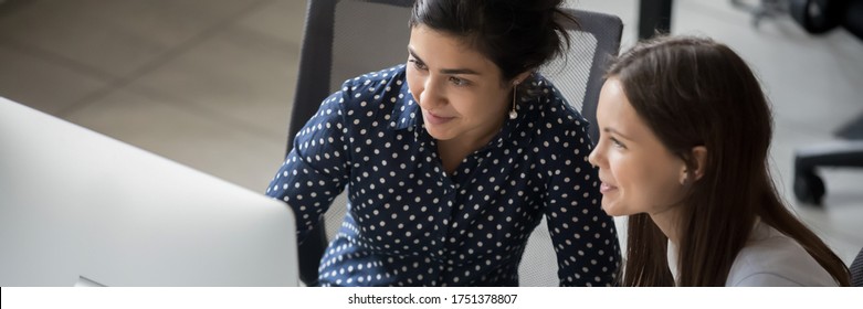 Multi ethnic female colleagues sit at workplace working together looks at pc screen use corporate program, apprentice listen mentor, teamwork concept. Horizontal photo banner for website header design
