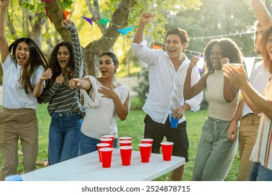 Multi ethnic friends cheering and having fun while playing beer pong at an outdoor party - Powered by Shutterstock