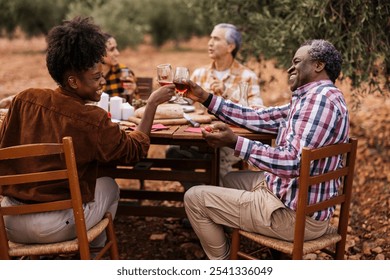 Multi ethnic group of farmers enjoying a celebratory meal with red wine amidst the olive grove, toasting to a successful harvest season - Powered by Shutterstock