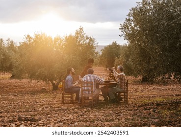 Multi ethnic group of farmers enjoying lunch together at a wooden table in a beautiful olive grove at sunset, celebrating the harvest and the fruits of their labor - Powered by Shutterstock