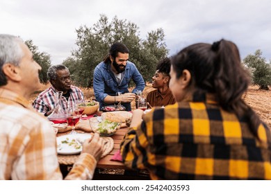 Multi ethnic group of farmers enjoying a healthy lunch together at a table in an olive grove, celebrating after the olive harvest - Powered by Shutterstock