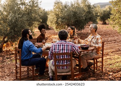 Multi ethnic group of farmers enjoying a healthy lunch together at a wooden table in an olive grove, celebrating the successful harvest with smiles and conversation - Powered by Shutterstock