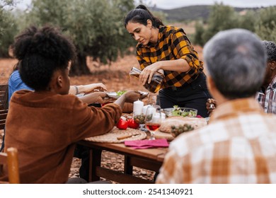 Multi ethnic group of farmers and workers are having lunch together at a table in the middle of an olive grove, celebrating the end of the harvest season by pouring fresh olive oil on a salad - Powered by Shutterstock