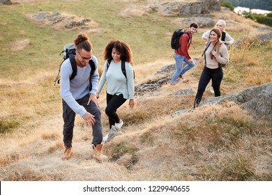 A multi ethnic group  of five young adult friends smile while climbing to the summit during a mountain hike, close up