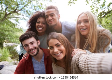 Multi ethnic group of five young adult friends pose to camera while taking a selfie during a break in a hike