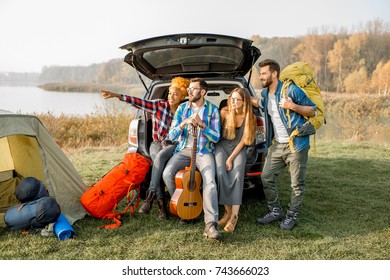 Multi ethnic group of friends sitting at the car trank during the outdoor recreation with tent and hiking equipment near the forest - Shutterstock ID 743666023