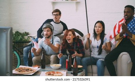 Multi Ethnic Group Of Friends Sports Fans With USA National Flags Watching Winter Olympic Games On TV Together Cheering Up Favourite Team At Home Indoors