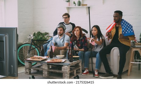 Multi Ethnic Group Of Friends Sports Fans With USA National Flags Watching Hockey Championship On TV Together Cheering Up Their Favourite Team At Home Indoors