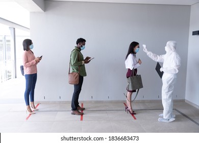 Multi Ethnic Group Of Male And Female Coworkers Wearing Face Masks Have Temperature Checked Before Entering Office. Hygiene And Social Distancing In Workplace During Coronavirus Covid 19 Pandemic.