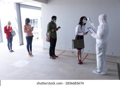 Multi Ethnic Group Of Male And Female Coworkers Wearing Face Masks Have Temperature Checked Before Entering Office. Hygiene And Social Distancing In Workplace During Coronavirus Covid 19 Pandemic.