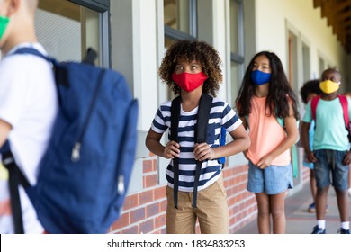 Multi Ethnic Group Of School Children Wearing Face Masks, Standing In Line, Having Their Temperature Checked By A Teacher. Education Back To School Health Safety During Covid19 Coronavirus Pandemic.