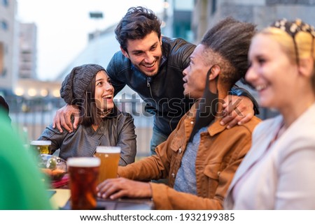 multi ethnic group of students chatting around a table in a brewery, gathering of young people during afternoon hours due curfew, restrictive health measures to prevent the spread of the corona virus
