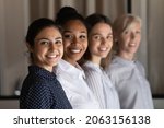 Multi ethnic group of successful confident women office workers professional experts stand in row one after another look at camera. Selective focus on young indian female team leader headshot portrait